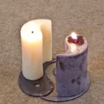 A candle is lit on the floor next to a metal object.
