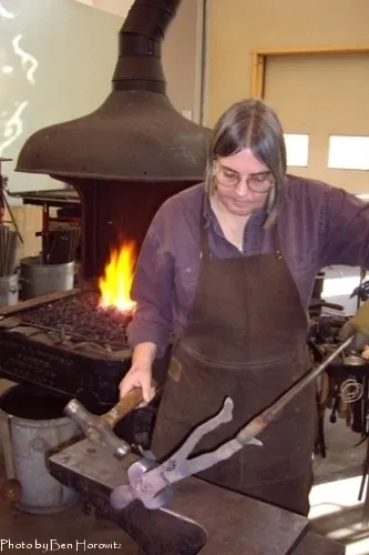 A woman in an apron working on metal.