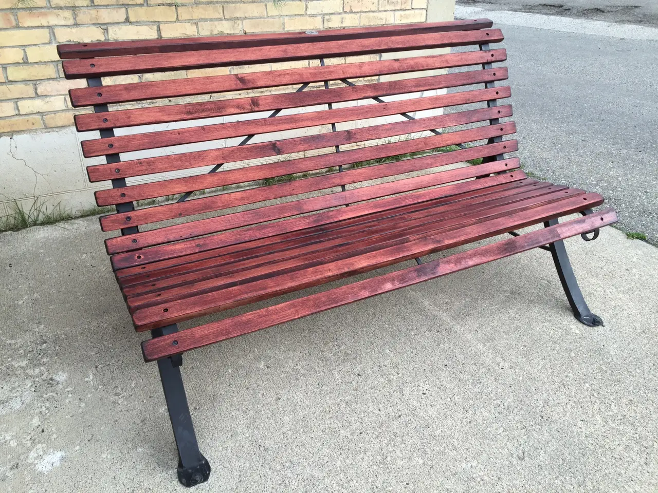 A wooden bench sitting on the side of a road.