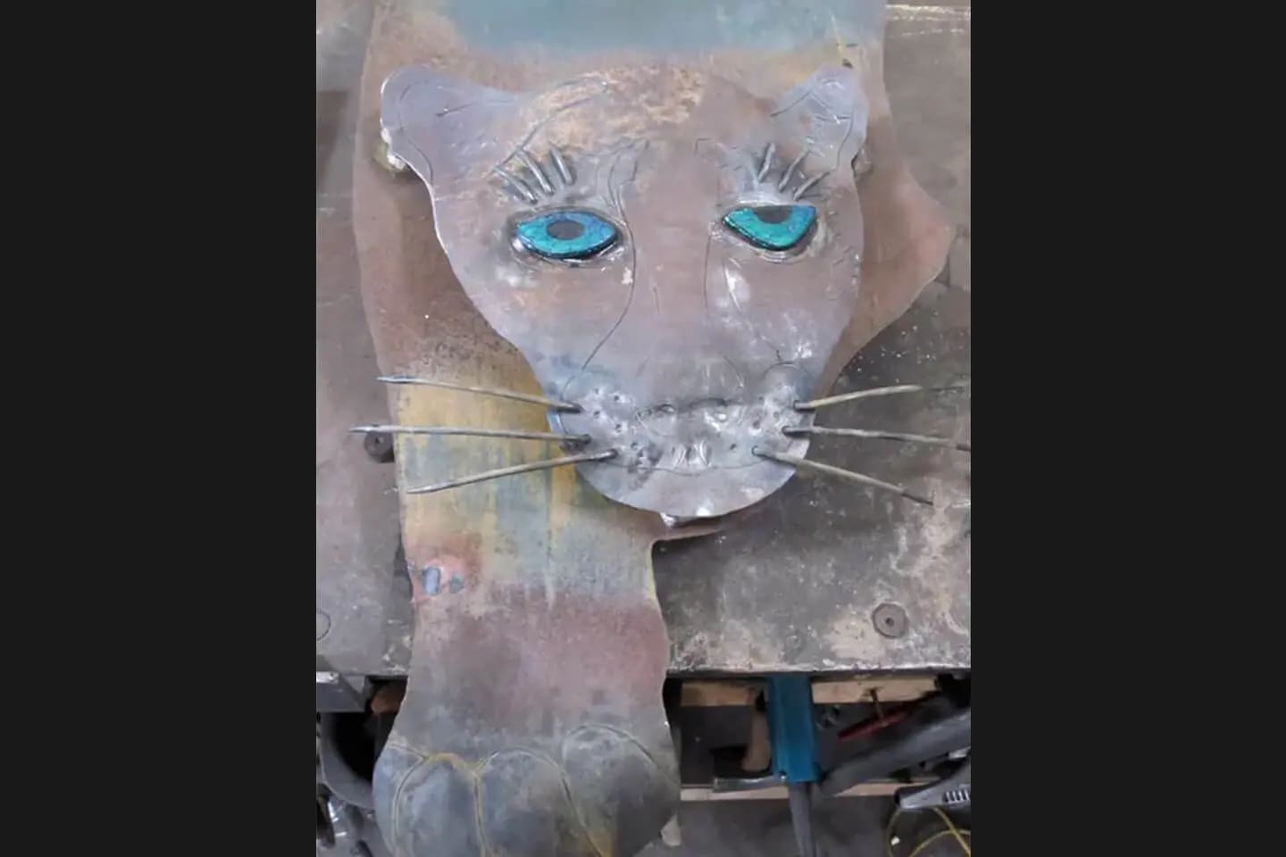 A cat sculpture with blue eyes and some paint on it.